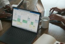 Three people in a meeting at a table discussing schedule on their Microsoft laptop