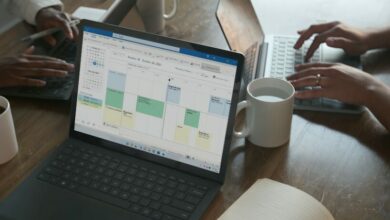 Three people in a meeting at a table discussing schedule on their Microsoft laptop