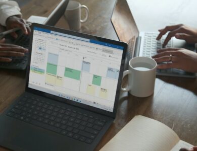 Three people in a meeting at a table discussing schedule on their Microsoft laptop