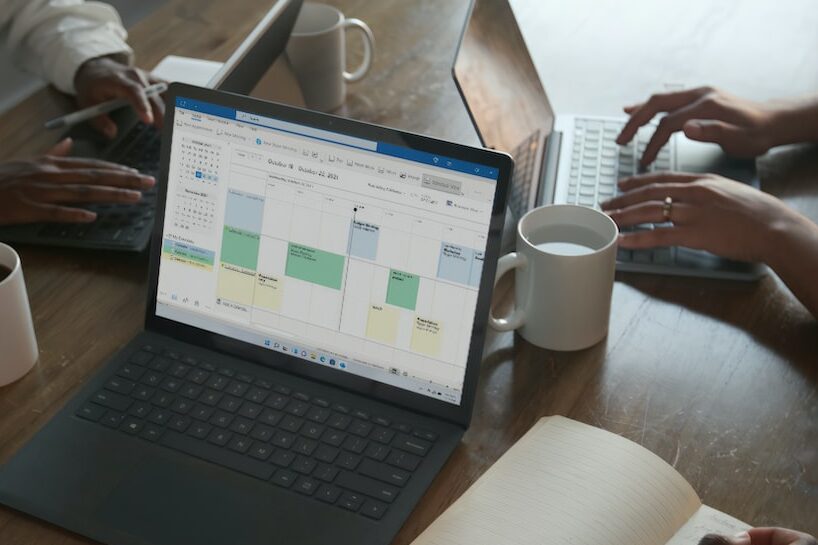 Three people in a meeting at a table discussing schedule on their Microsoft laptop