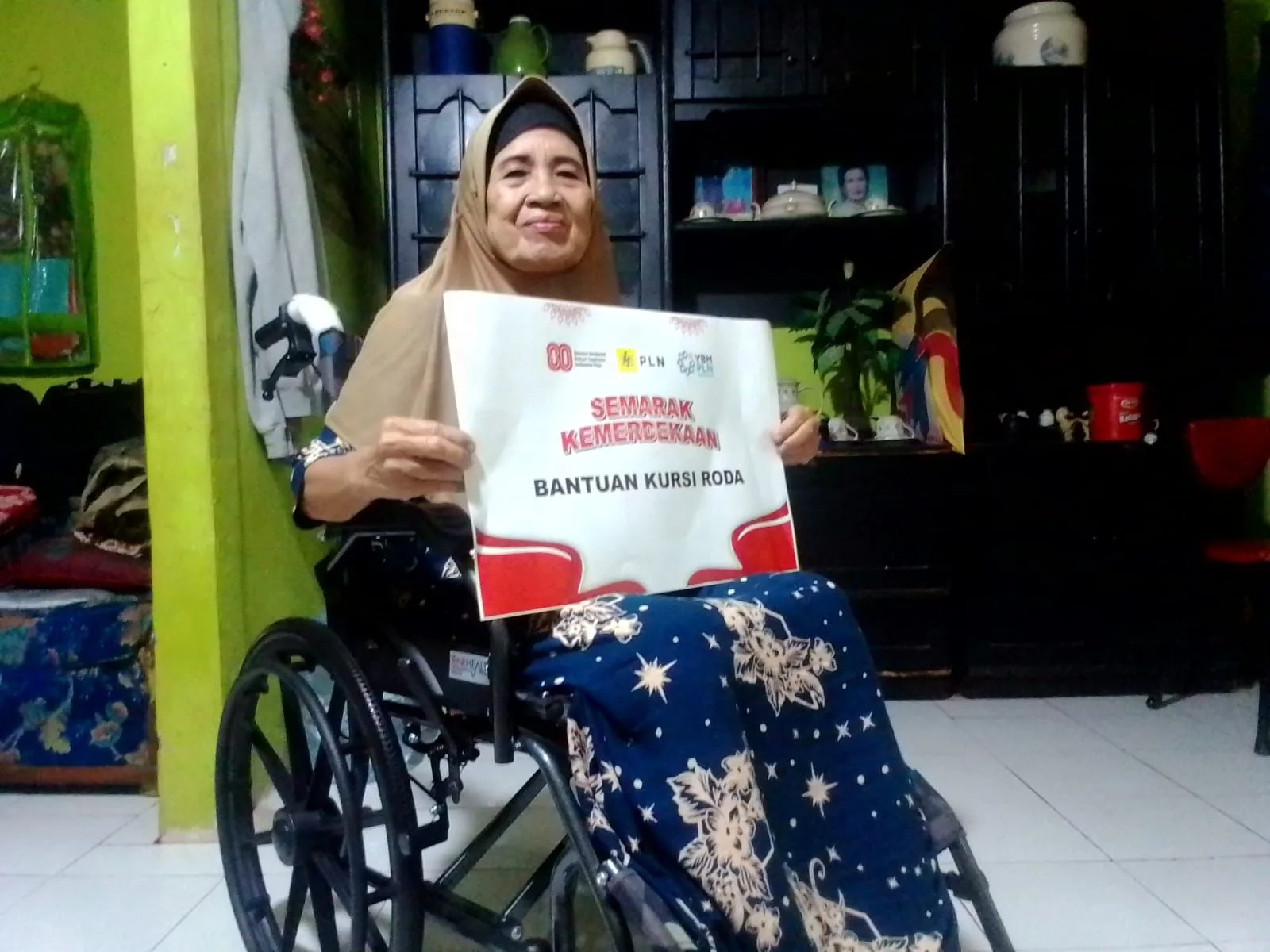 Wujud kepedulian di momen kemerdekaan. Ibu penerima bantuan kursi roda dari PLN dan OJK.