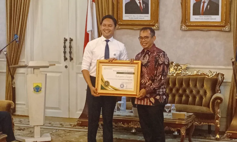 Bupati Cianjur, dr. M Wahyu Ferdian (kiri), saat menerima piagam penghargaan Universal Health Coverage (UHC) Prioritas dari Direktur Utama BPJS, David Bangun, Jumat (26/9/2025). Pencapaian ini menjadi penanda bahwa seluruh warga Cianjur kini dapat berobat gratis hanya dengan KTP.