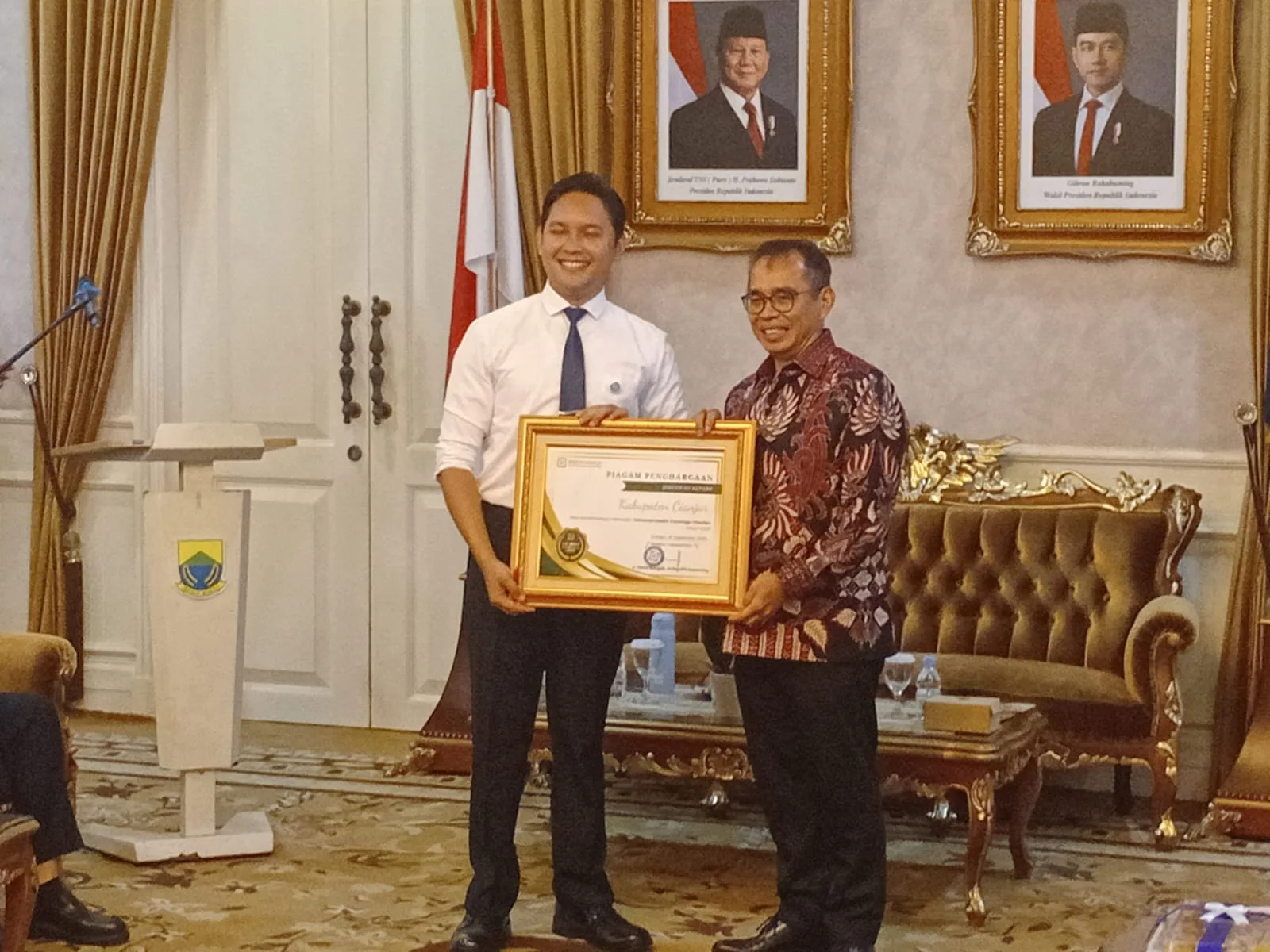 Bupati Cianjur, dr. M Wahyu Ferdian (kiri), saat menerima piagam penghargaan Universal Health Coverage (UHC) Prioritas dari Direktur Utama BPJS, David Bangun, Jumat (26/9/2025). Pencapaian ini menjadi penanda bahwa seluruh warga Cianjur kini dapat berobat gratis hanya dengan KTP.