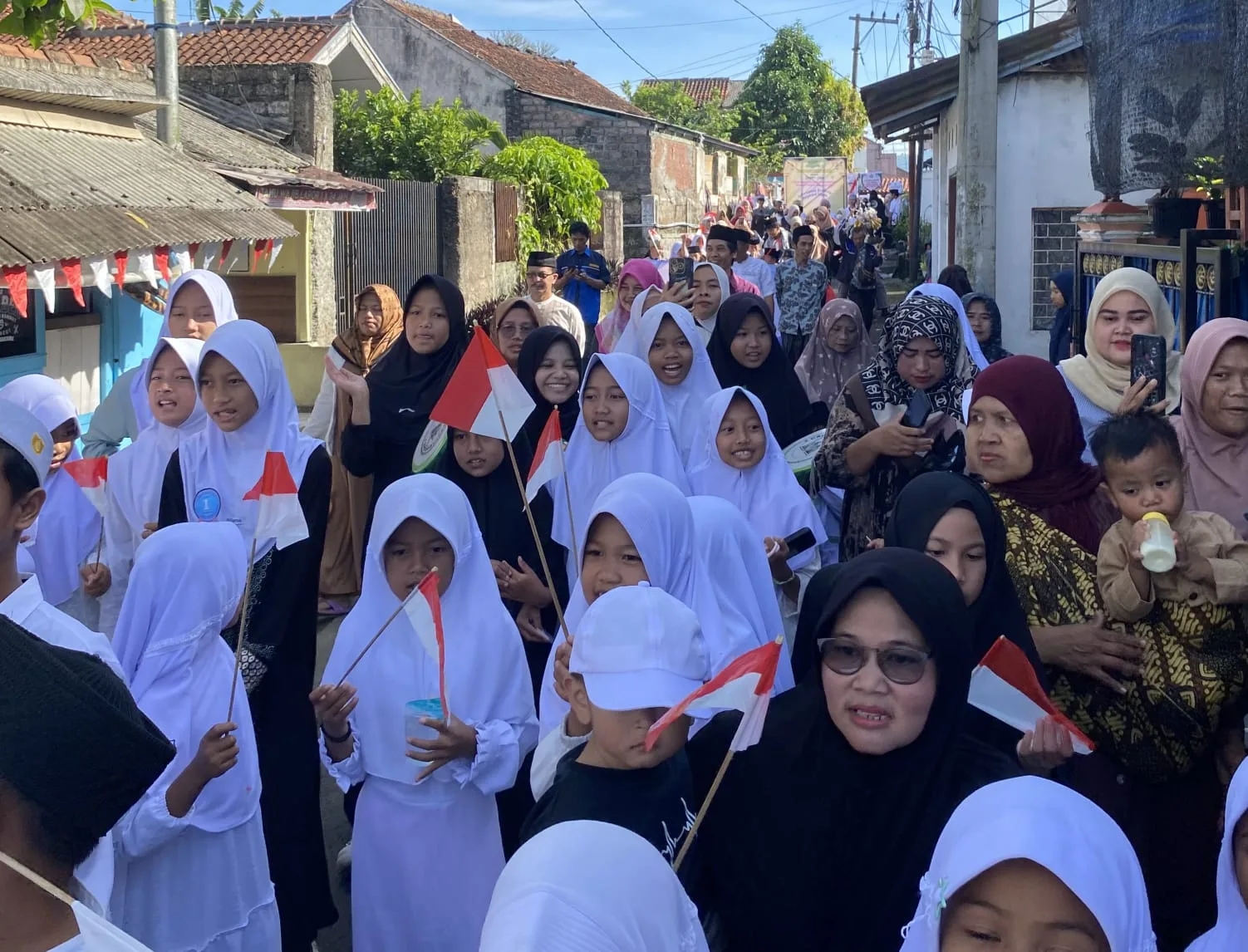 SEMARAK HARI SANTRI: Para santri dan warga Desa Sukamanah mengikuti pawai di lingkungan desa sambil membawa bendera Merah Putih untuk memeriahkan rangkaian peringatan Hari Santri Nasional 2025, Minggu (26/10/25).