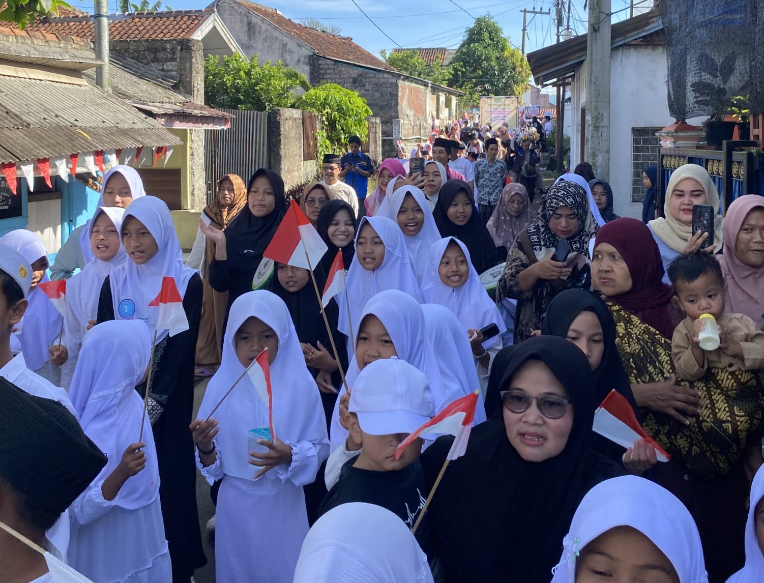 SEMARAK HARI SANTRI: Para santri dan warga Desa Sukamanah mengikuti pawai di lingkungan desa sambil membawa bendera Merah Putih untuk memeriahkan rangkaian peringatan Hari Santri Nasional 2025, Minggu (26/10/25).