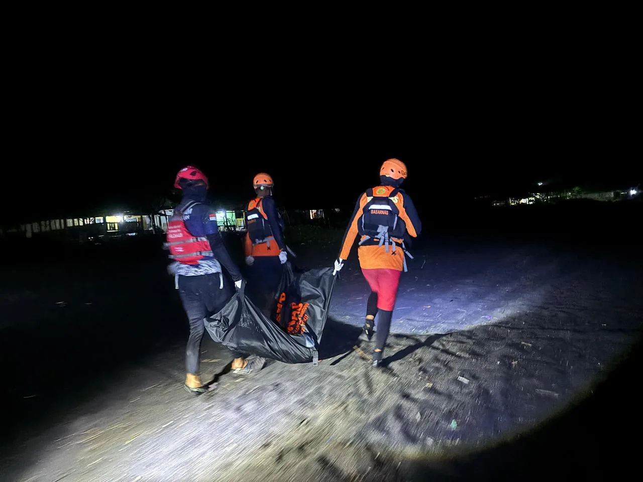 Petugas tim SAR gabungan menggotong kantong jenazah saat melakukan penyisiran dan evakuasi di area pantai pada malam hari.