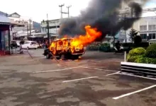 Sebuah minibus ludes terbakar di area parkir, memicu kepulan asap hitam tebal yang membubung ke udara.