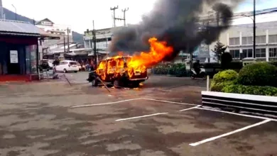 Sebuah minibus ludes terbakar di area parkir, memicu kepulan asap hitam tebal yang membubung ke udara.