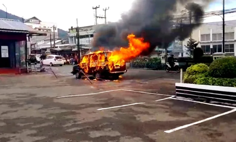 Sebuah minibus ludes terbakar di area parkir, memicu kepulan asap hitam tebal yang membubung ke udara.