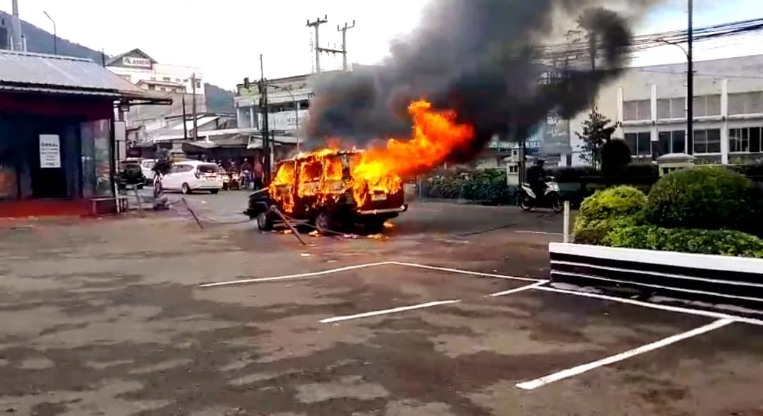 Sebuah minibus ludes terbakar di area parkir, memicu kepulan asap hitam tebal yang membubung ke udara.