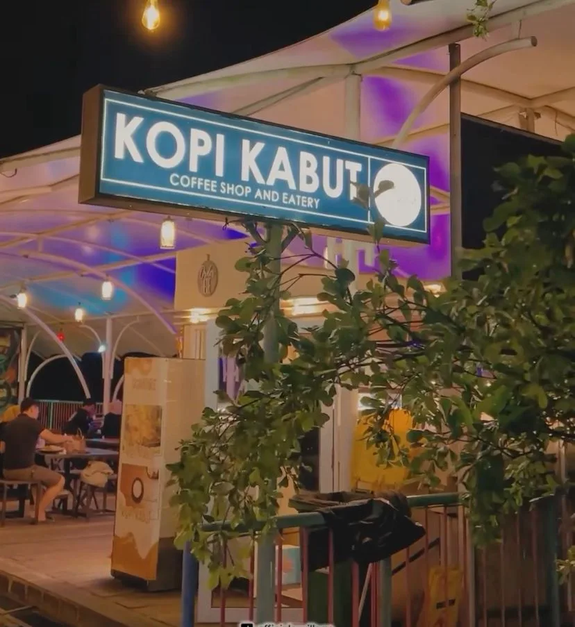 SUASANA malam di Kopi Kabut Coffee Shop and Eatery. Papan nama kafe yang menyala terang menyambut pengunjung yang tengah menikmati waktu bersantai.
