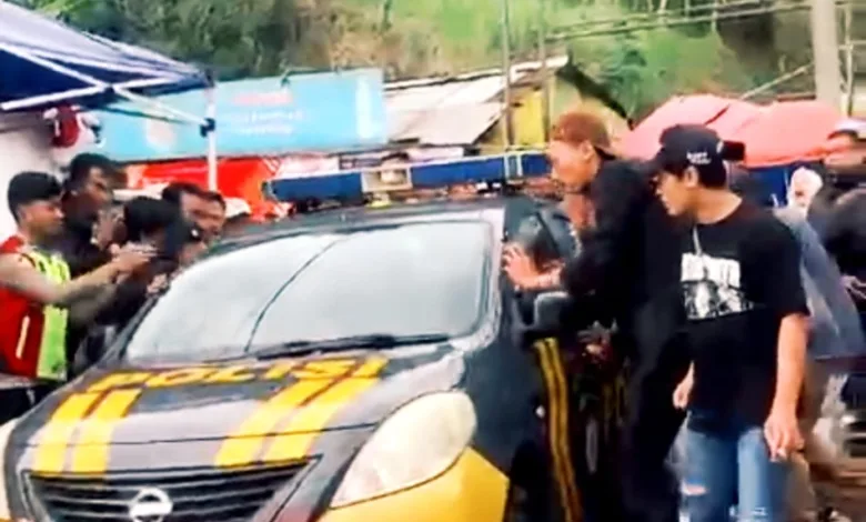 Mobil patroli Polsek Pacet saat mengevakuasi juru parkir berinisial E (30) dari kepungan warga di Rest Area Segar Alam, Puncak, Cianjur, Sabtu (27/12/2025).