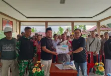 Kepala Desa Sukamanah, Indra Surya Pradana (kiri), menyerahkan secara simbolis donasi 1,5 ton beras kepada Pimpinan Cianjur Update, Indra Arfiandi (kanan), disaksikan oleh Babinsa dan unsur RT/RW di Aula Agro Edu Wisata Tani Arta Sukamanah, Sabtu (13/12/2025).