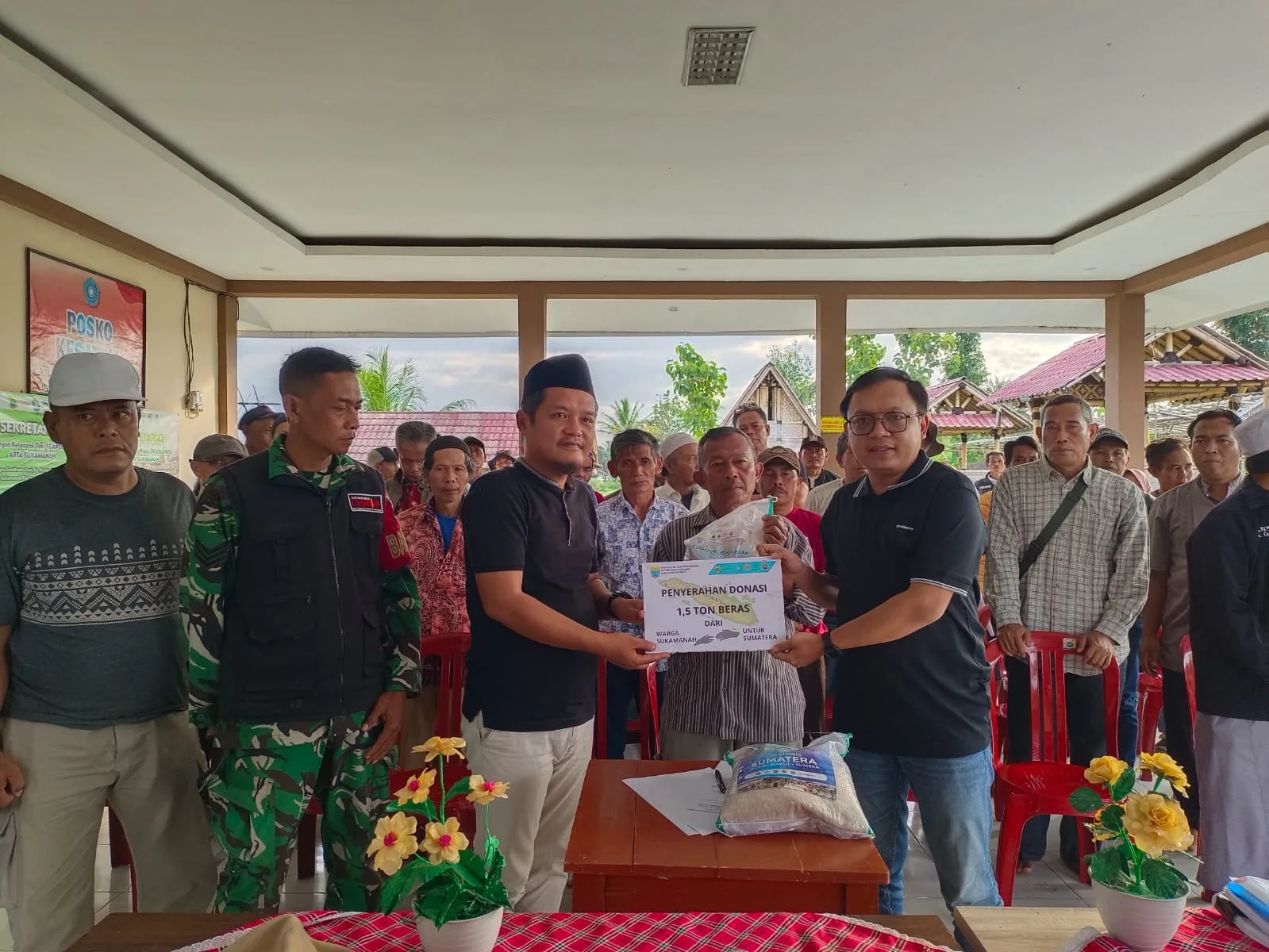 Kepala Desa Sukamanah, Indra Surya Pradana (kiri), menyerahkan secara simbolis donasi 1,5 ton beras kepada Pimpinan Cianjur Update, Indra Arfiandi (kanan), disaksikan oleh Babinsa dan unsur RT/RW di Aula Agro Edu Wisata Tani Arta Sukamanah, Sabtu (13/12/2025).