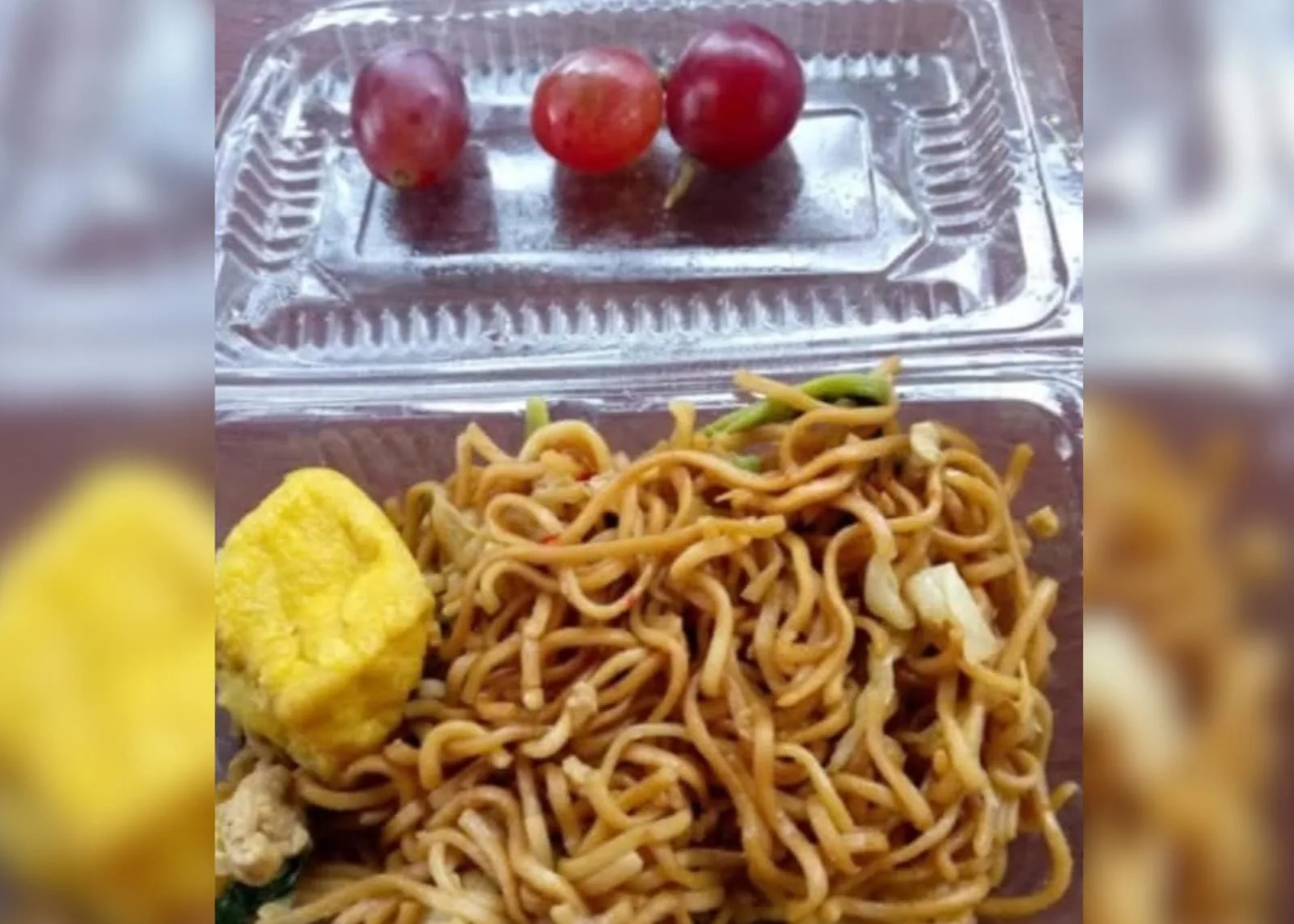 Menu Makan Bergizi Gratis (MBG) di Cianjur yang dikeluhkan orang tua murid: Mi goreng, satu potong tahu kuning, dan hanya tiga butir anggur, disajikan dalam kemasan mika plastik.