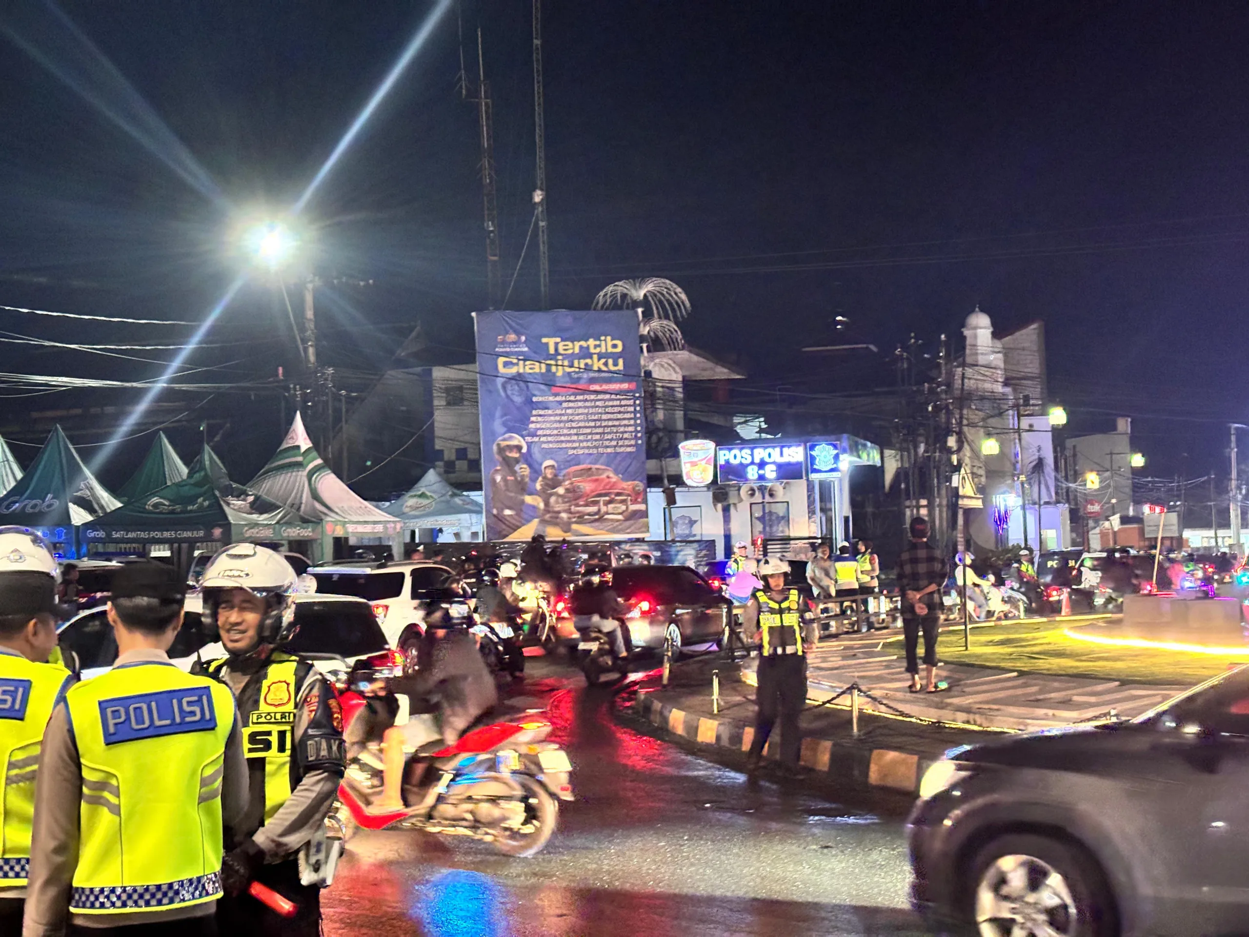 Petugas kepolisian mengatur arus lalu lintas di Bundaran Tugu Lampu Gentur, Cianjur, Rabu malam (31/12/2025), menyusul penutupan jalur menuju Puncak secara situasional menjelang pergantian Tahun Baru untuk mengurai kepadatan kendaraan.