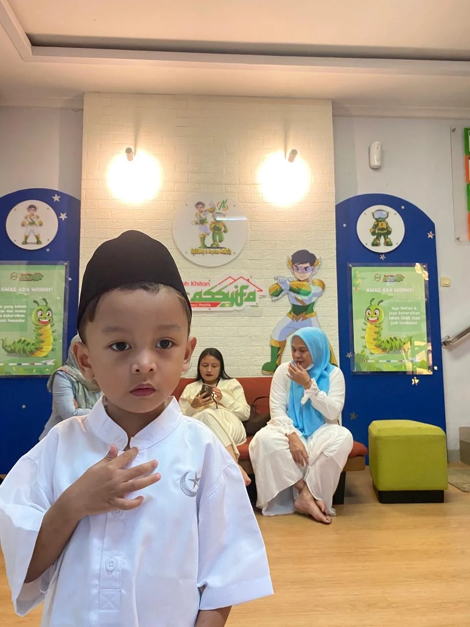 "Jagoan Kecil Siap Dewasa." Mengenakan koko putih dan peci hitam, Muhammad Eshar Rumi berdiri gagah dengan ekspresi percaya diri di area Klinik Nur Assyifa.